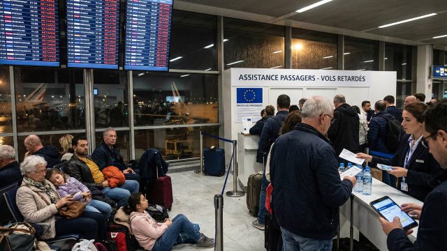 Voyageurs fatigués et familles patientant dans un terminal de l'aéroport Charles de Gaulle tard la nuit, illustrant les désagréments causés par les retards de vols nocturnes et l'attente d'assistance.