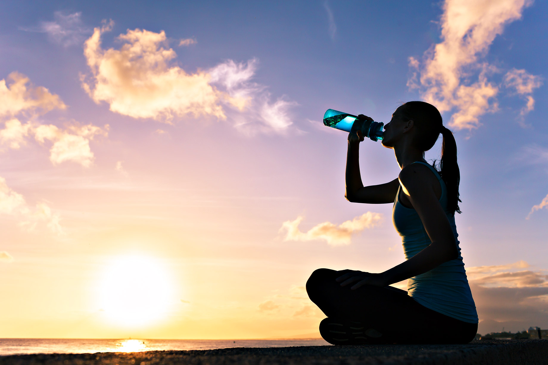 Woman Drinking Water On The Beach At Sunset