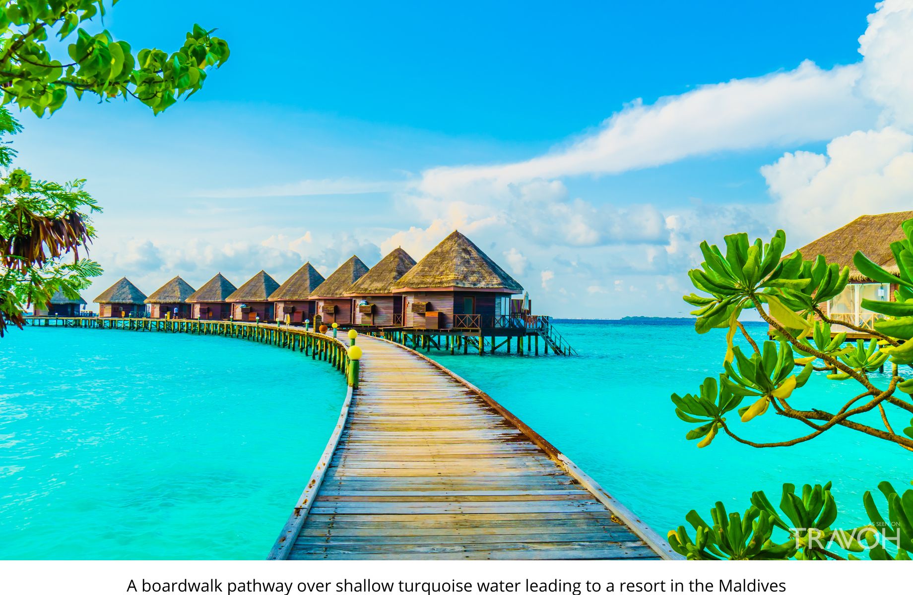 A boardwalk pathway over shallow turquoise water leading to a resort in the Maldives