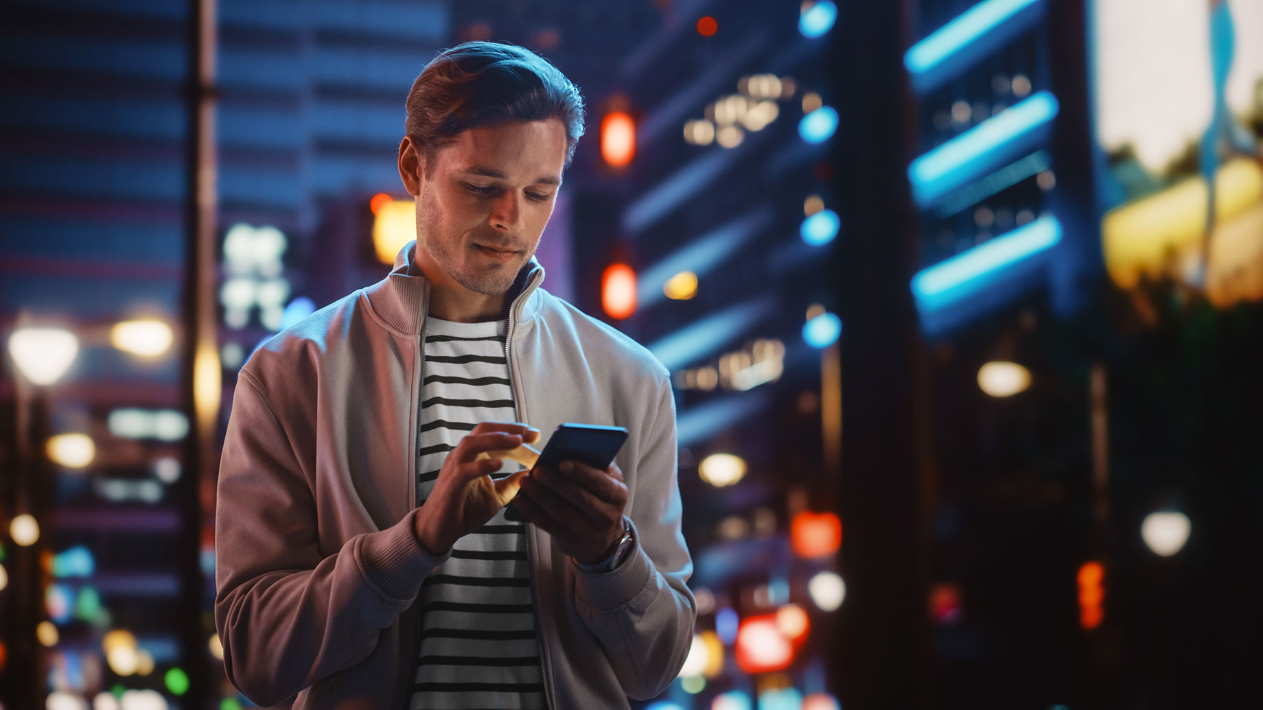 Man Using His Smartphone While Walking Through A City At Night