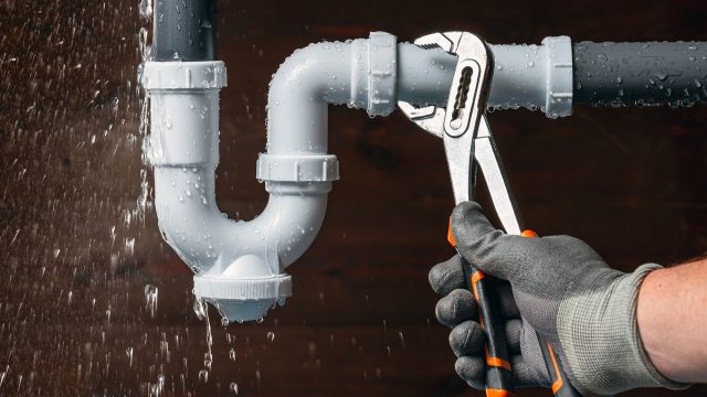 Plumber Using a Wrench on a Pipe with a Water Leak