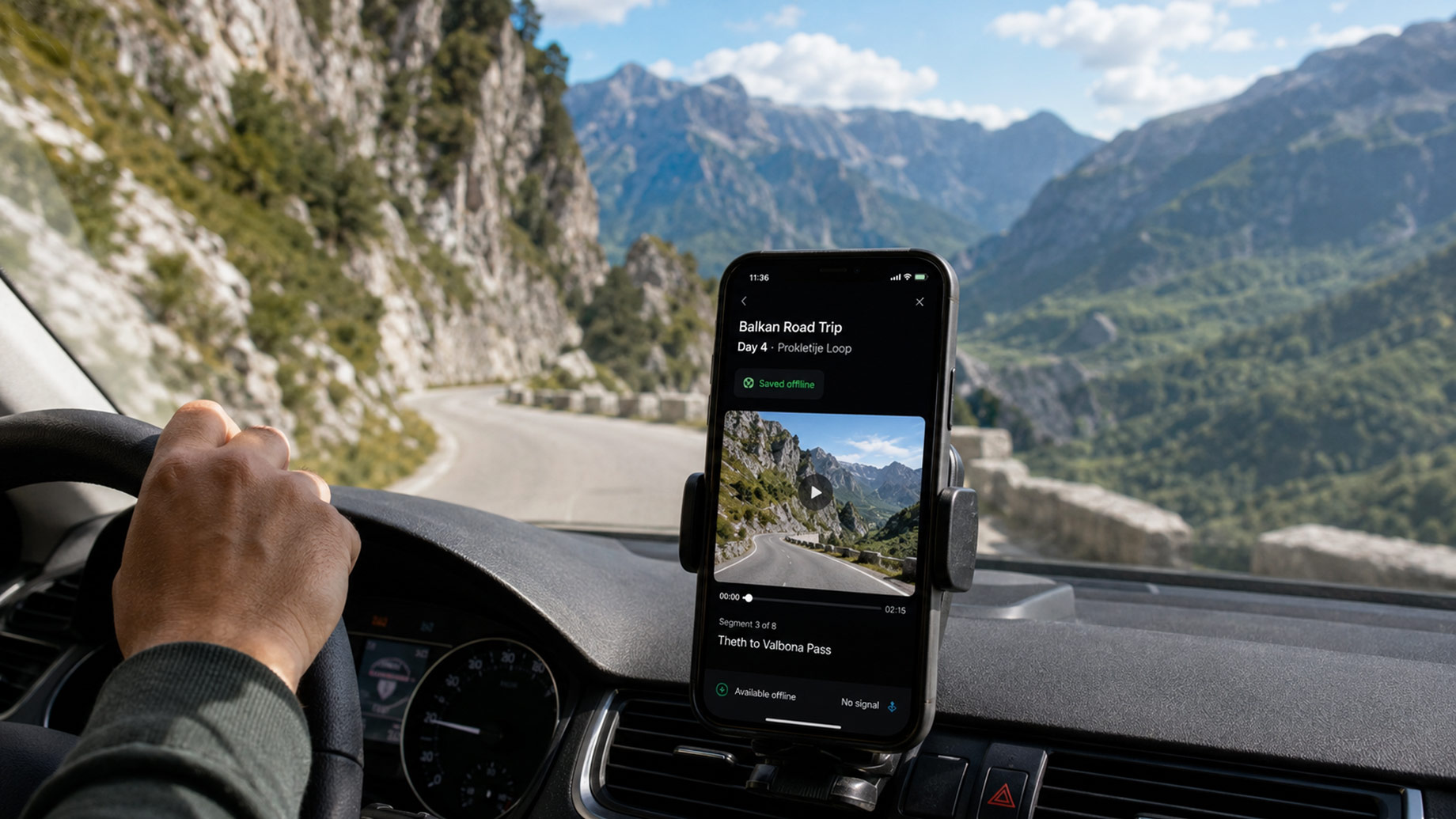 Smartphone displaying a saved offline route clip while a driver navigates a winding mountain pass through the Albanian Alps.