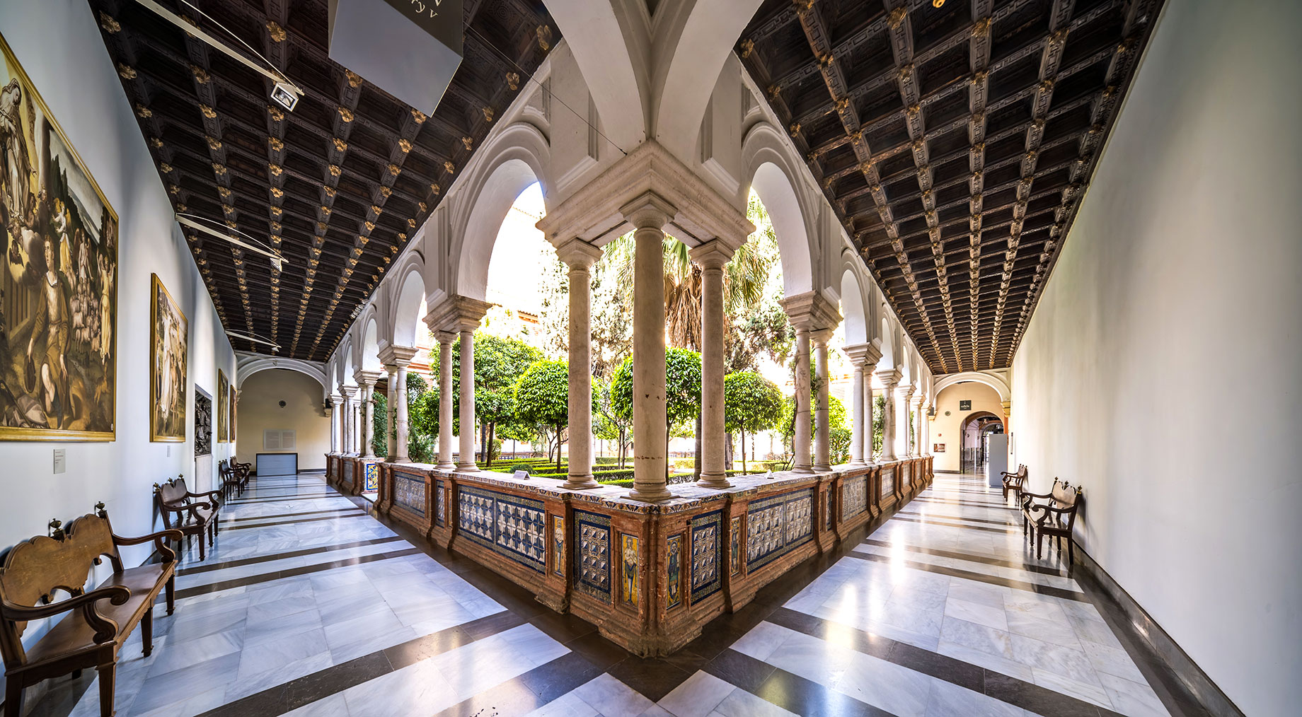 Arched cloister with decorative tiles, paintings and a garden courtyard at the Museo de Bellas Artes in Seville, Spain.